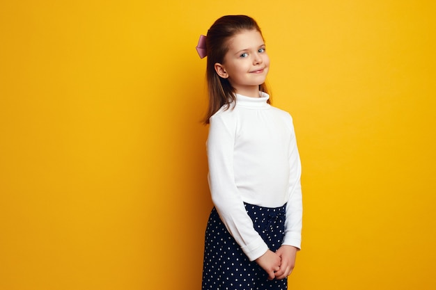 Graziosa bambina in dolcevita bianco in posa adorabile su sfondo giallo