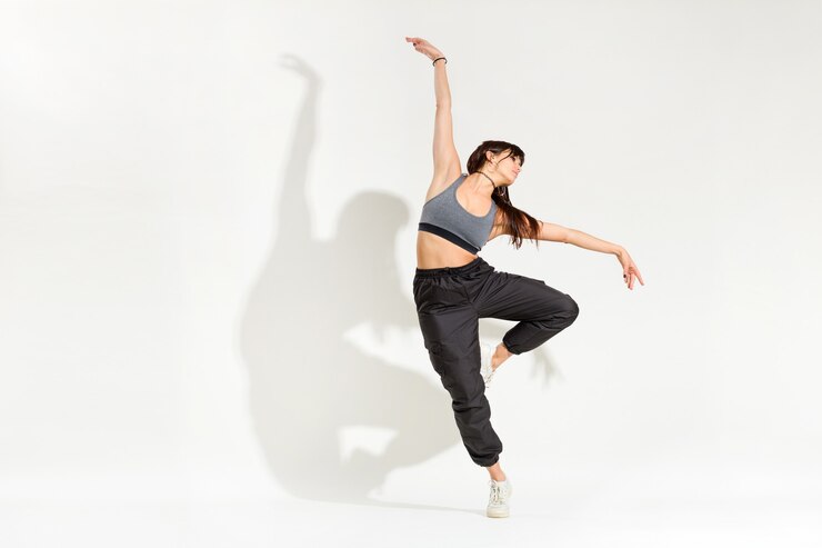 Foto graziosa giovane donna ballerina in un vestito hip hop eseguendo una posa di danza classica con le braccia tese in equilibrio su una gamba con ombra artistica su uno sfondo bianco studio