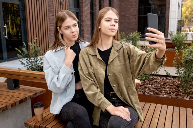 Graziosi gemelli adolescenti che si fanno selfie seduti sulla panchina