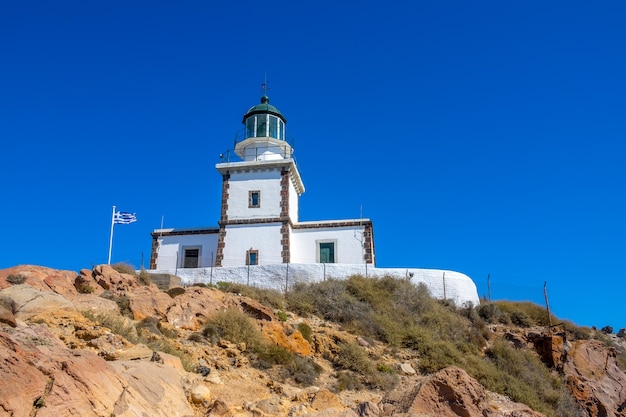 Grecia. Montagna rocciosa in una giornata senza nuvole. Costruzione del faro contro il cielo blu e la bandiera nazionale