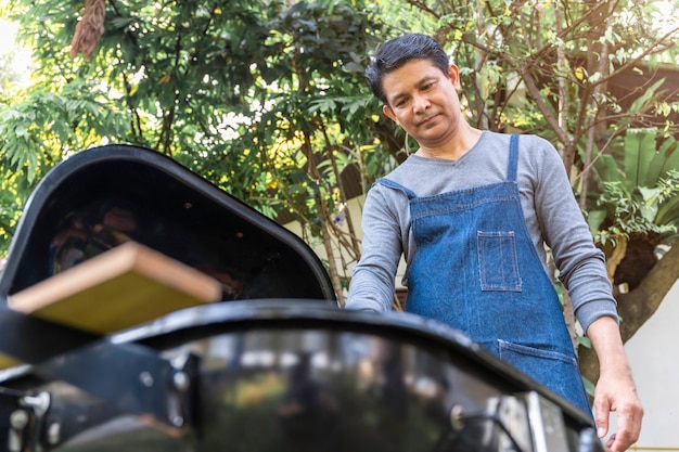 Grembiule d'uso dell'uomo asiatico senior e fare un barbecue nel parco.