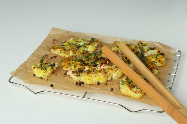 Griglia da forno con cavolfiore al forno e pinze di legno su sfondo bianco.