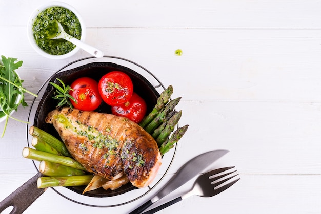 Griglia del petto di pollo con le verdure del bbq e la salsa di pesto in una padella del ghisa su bianco