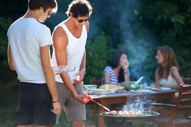 Grigliare la carne alla perfezione Giovani ragazzi che grigliano carne alla griglia all'aperto Stile di vita