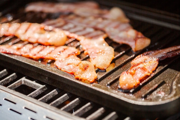 Grigliare le strisce di pancetta su una piastra in ghisa nel grill a gas all'aperto.