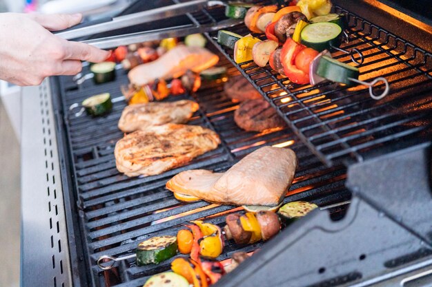 Grigliare un salmone atlantico, petto di pollo, spiedini di verdure e hamburger vegetariani su una griglia all'aperto.