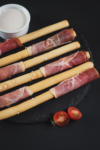 Grissini avvolti da prosciutto su sfondo nero