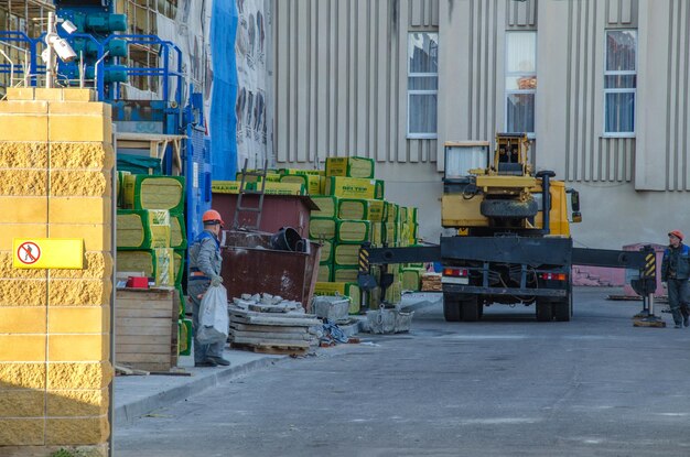 Grodno Bielorussia 11 ottobre 2018 Un uomo con casco e abbigliamento da lavoro Riscaldamento della facciata dell'edificio Si tratta di una gru a torre Nelle vicinanze si trova un materiale da costruzione