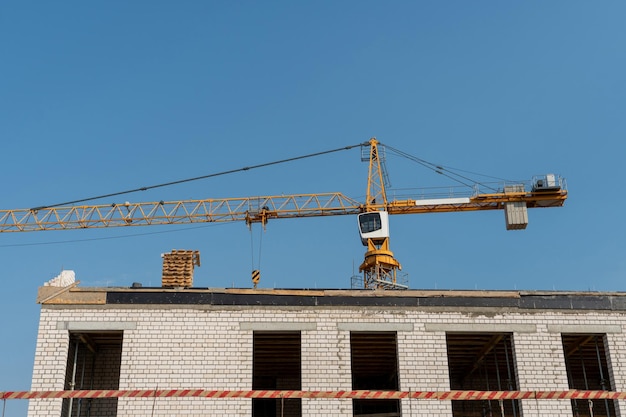 Gru a torre arancione contro un cielo blu chiaro Costruzione di un nuovo edificio in mattoni Cantiere moderno Housing on credit mutui vendita di immobili