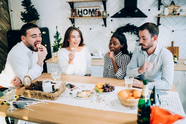 Gruppo allegro di amici che mangiano e bevono in cucina godendosi il fine settimana di Capodanno a casa