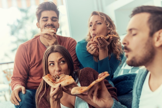 Gruppo allegro di amici che si divertono a casa, mangiando pizza.