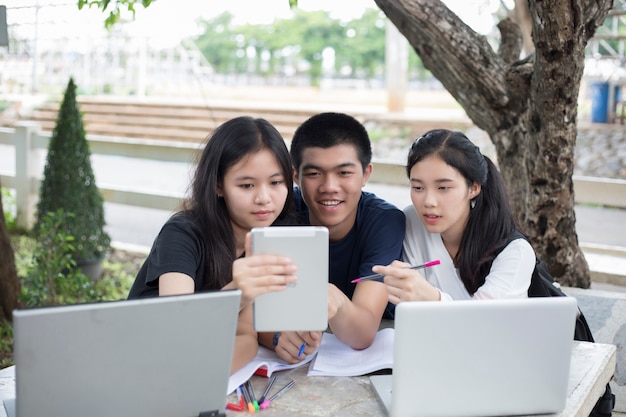 Gruppo asiatico di studenti che utilizzano tablet e notebook condividendo le idee per lavorare nel campus l