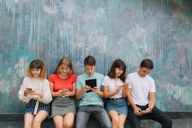 Gruppo di adolescenti seduti all&#39;aperto usando i loro telefoni cellulari.