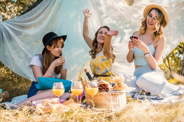 Gruppo di amiche che fanno picnic all'aperto. Si siedono, sorridono e giocano a carte