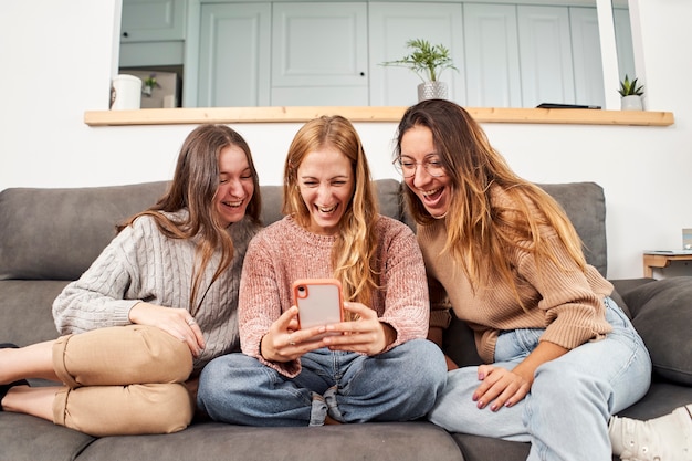 Gruppo di amiche sul divano di casa, utilizzando un telefono cellulare ridendo