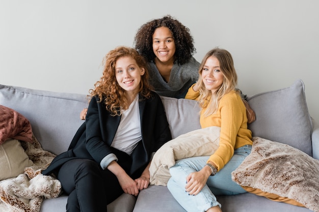 Gruppo di amichevoli ragazze interculturali in smart casual seduto sul divano