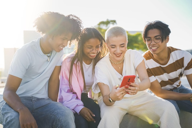 Gruppo di amici adolescenti felici che guardano il telefono e ridono per la strada della città