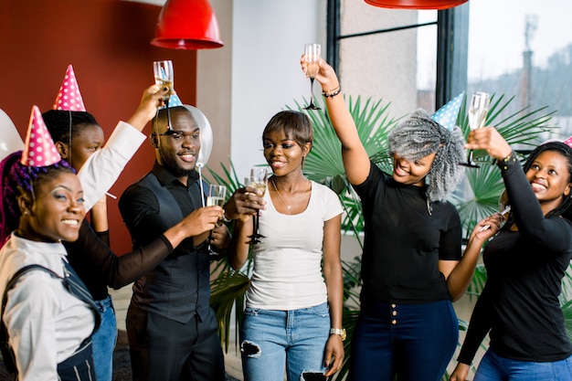 Gruppo di amici africani felici che bevono champagne e che celebrano la festa di compleanno