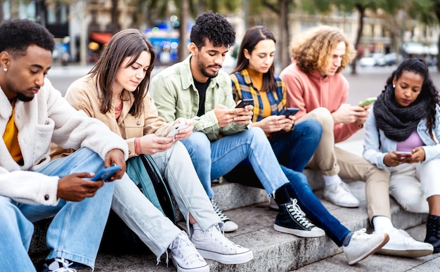 Gruppo di amici annoiati che utilizzano lo smartphone mobile seduto nel cortile del college universitario - Giovani dipendenti dai dispositivi smartphone - Concetto di tecnologia con studenti sempre connessi su un filtro luminoso e vivido