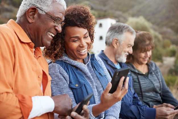 Gruppo di amici anziani in escursione in campagna guardando i cellulari insieme