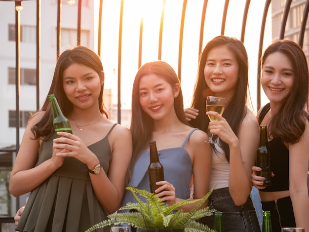 Gruppo di amici asiatici tifo e bere alla festa in terrazza. Giovani che godono e che vanno in giro sul tetto al tramonto