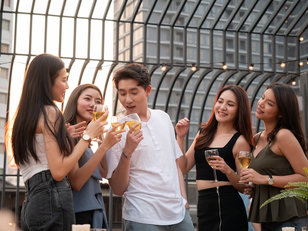 Gruppo di amici asiatici tifo e bere alla festa in terrazza. Giovani che godono e che vanno in giro sul tetto al tramonto