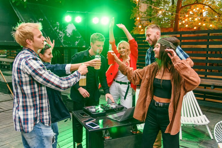 Gruppo di amici che bevono birra, ballano al ritmo della musica, chiacchierano e si divertono alla festa estiva all'aperto.