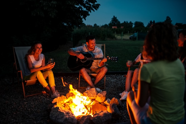 Gruppo di amici che godono di musica intorno al firepit di notte.