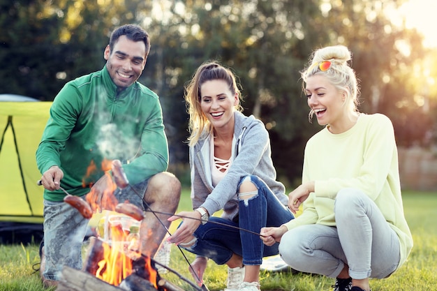 gruppo di amici che preparano salsicce sul fuoco