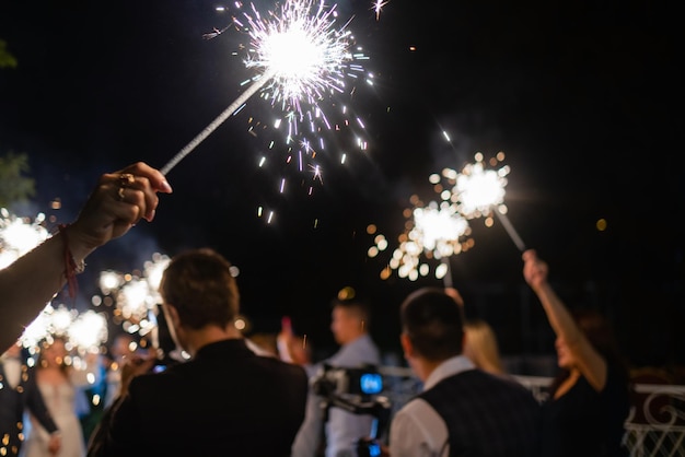 Gruppo di amici che si divertono con le stelle filanti giovani uomini e donne che si divertono con i fuochi d'artificio