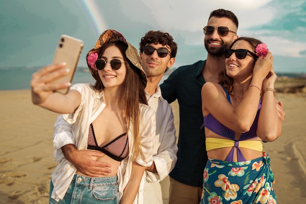 Gruppo di amici che si fanno un selfie sulla spiaggia contro un bellissimo arcobaleno