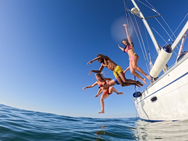 Gruppo di amici che si tuffano in acqua durante un'escursione in barca a vela giovani che saltano all'interno dell'oceano durante le vacanze estive da una vela divertendosi stile di vita di vacanza di lusso