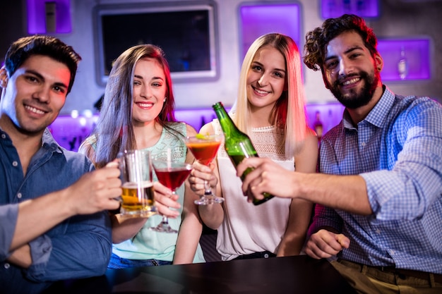 Gruppo di amici che tostano cocktail, bottiglia di birra e bicchiere di birra al bancone del bar