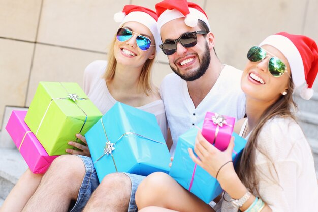 gruppo di amici con i cappelli di Babbo Natale seduti in città con regali