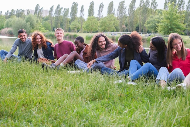 Gruppo di amici di diverse culture seduti sull'erba all'aperto nel parco al tramonto Concetto Diversità del legame di stile di vita