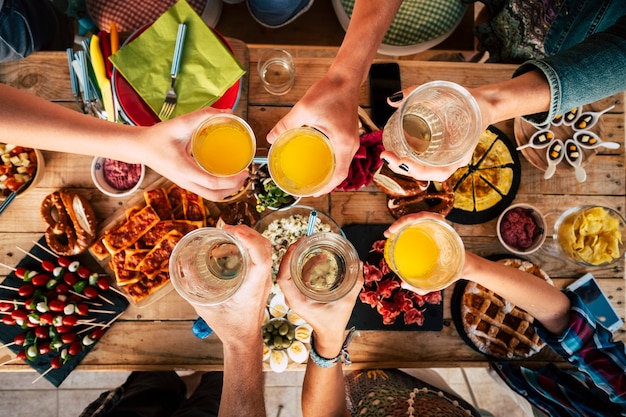 Gruppo di amici di età mista generazioni, dai bambini agli adulti, si divertono insieme a cibo e bevande - vista aerea dall'alto del tavolo e persone che brindano insieme in amicizia - concetto di casa o ristorante