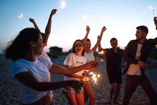 Gruppo di amici di notte sulla spiaggia con stelle filanti Giovani amici che si divertono in vacanza al mare