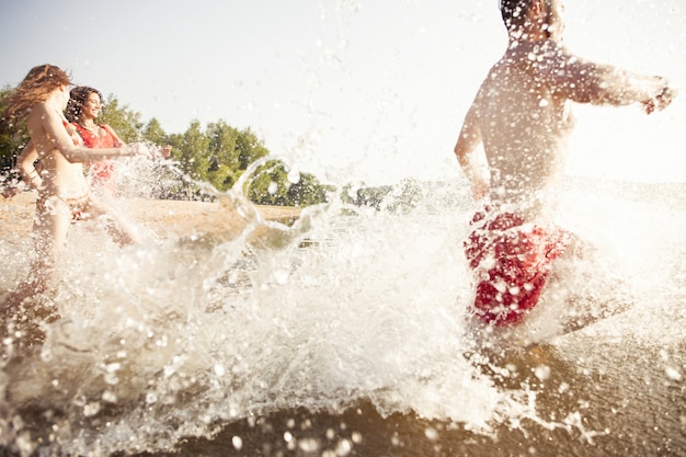 Gruppo di amici felici che corrono in acqua - persone attive che si divertono sulla spiaggia in vacanza - turisti che vanno a nuotare