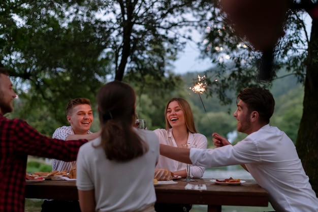 gruppo di amici felici che fanno picnic con cena francese all'aperto durante le vacanze estive vicino al fiume in una natura meravigliosa