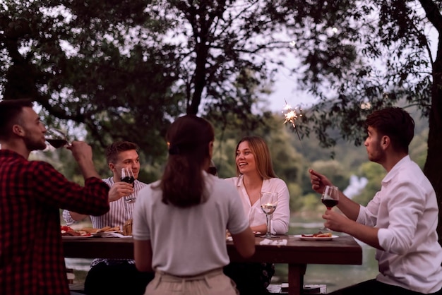 gruppo di amici felici che fanno picnic con cena francese all'aperto durante le vacanze estive vicino al fiume in una natura meravigliosa