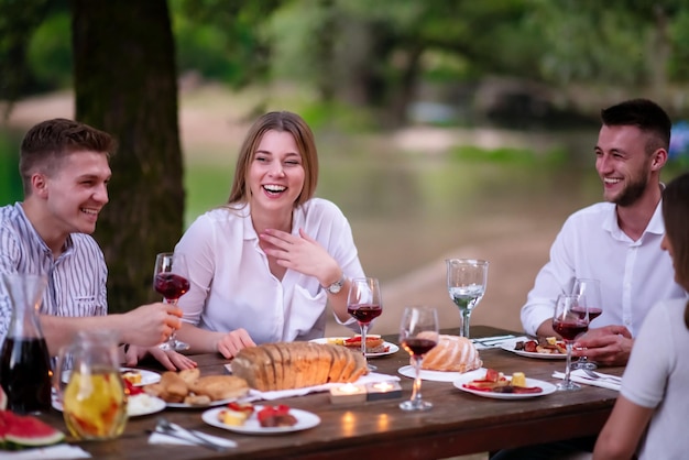 gruppo di amici felici che fanno picnic con cena francese all'aperto durante le vacanze estive vicino al fiume in una natura meravigliosa