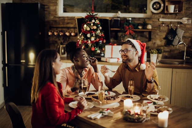 Gruppo di amici felici che mangiano dessert e parlano durante la cena di Natale a casa
