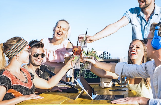 Gruppo di amici felici che tostano le bevande di moda al video streaming in diretta alla festa in spiaggia