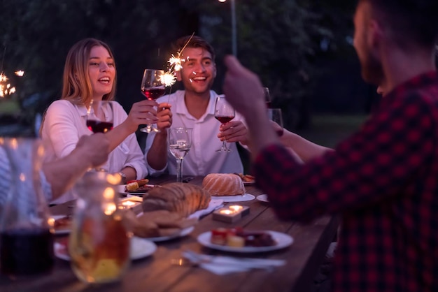 gruppo di amici felici che tostano un bicchiere di vino rosso mentre fanno un picnic con cena francese all'aperto durante le vacanze estive vicino al fiume in una natura meravigliosa