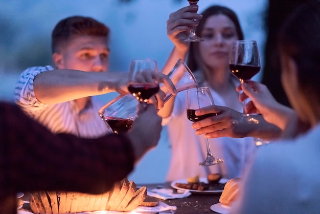 gruppo di amici felici che tostano un bicchiere di vino rosso mentre fanno un picnic con cena francese all'aperto durante le vacanze estive vicino al fiume in una natura meravigliosa