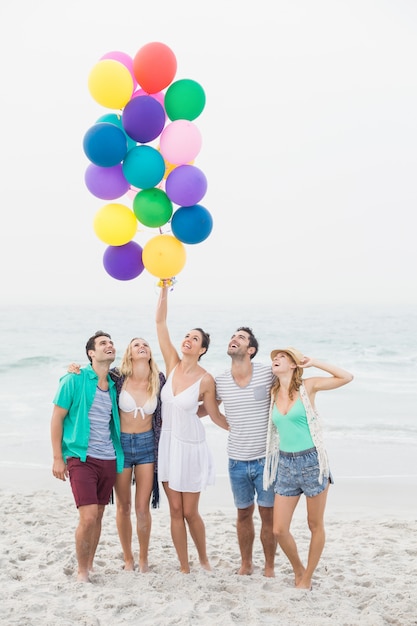 Gruppo di amici in piedi sulla spiaggia con palloncini