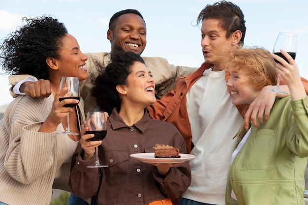 Gruppo di amici in posa con bicchieri di vino e torta durante la festa all'aperto