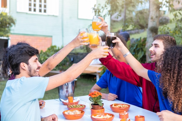 Gruppo di amici millenari che si divertono fuori a brindare bevande alla festa in giardino Concetto di stile di vita