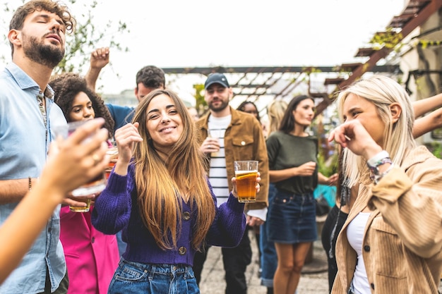 Gruppo di amici multirazziali che si divertono in una festa danzante sul tetto della generazione z studenti felici che si divertono e bevono