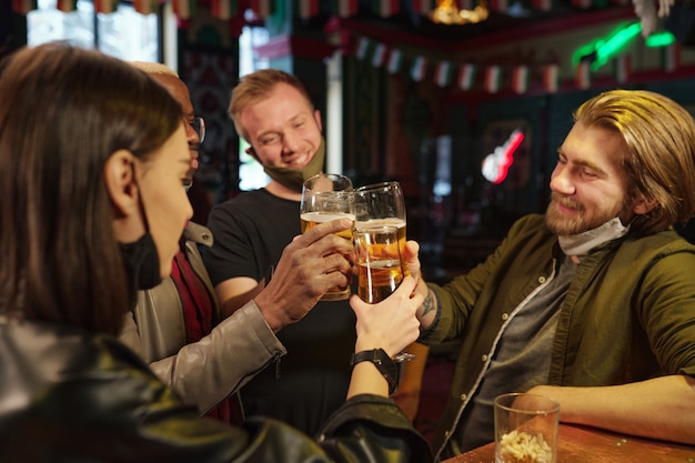 Gruppo di amici seduti a tavola che brindano con la birra al bar